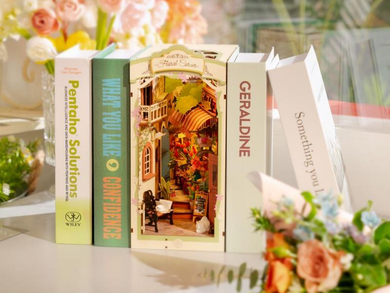 A glowing miniature library book nook kit between two hardcover books